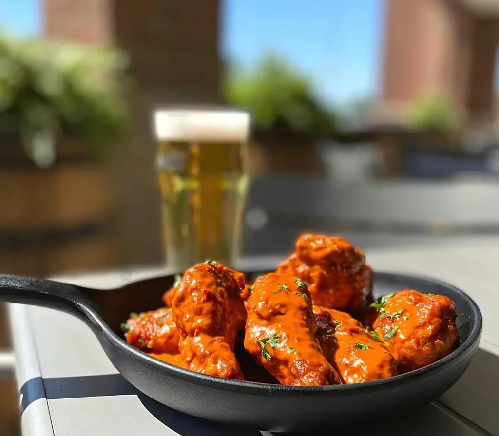 Orange-red chicken wings in cast iron skillet, garnished with green herbs.