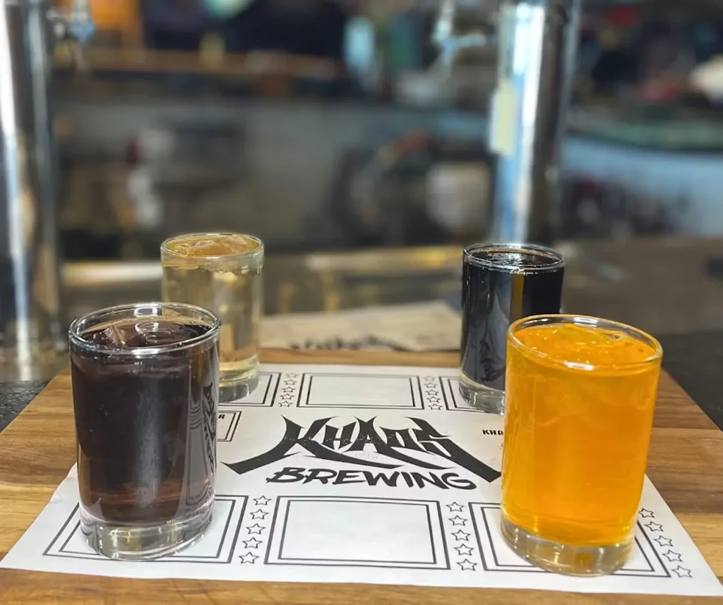 A flight of four different colored drinks on a KHAOS BREWING mat.