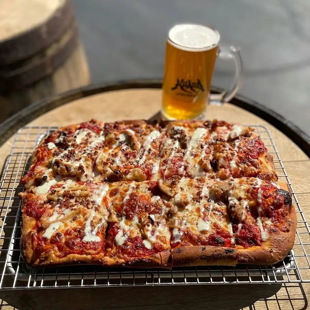 Sliced rectangular pizza with meat and mushrooms, on a rack, and beer.