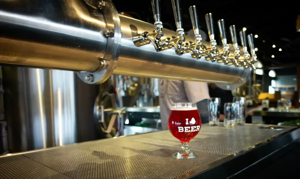 Stainless steel beer taps above an 'I ❤️ BEER' glass with red drink.