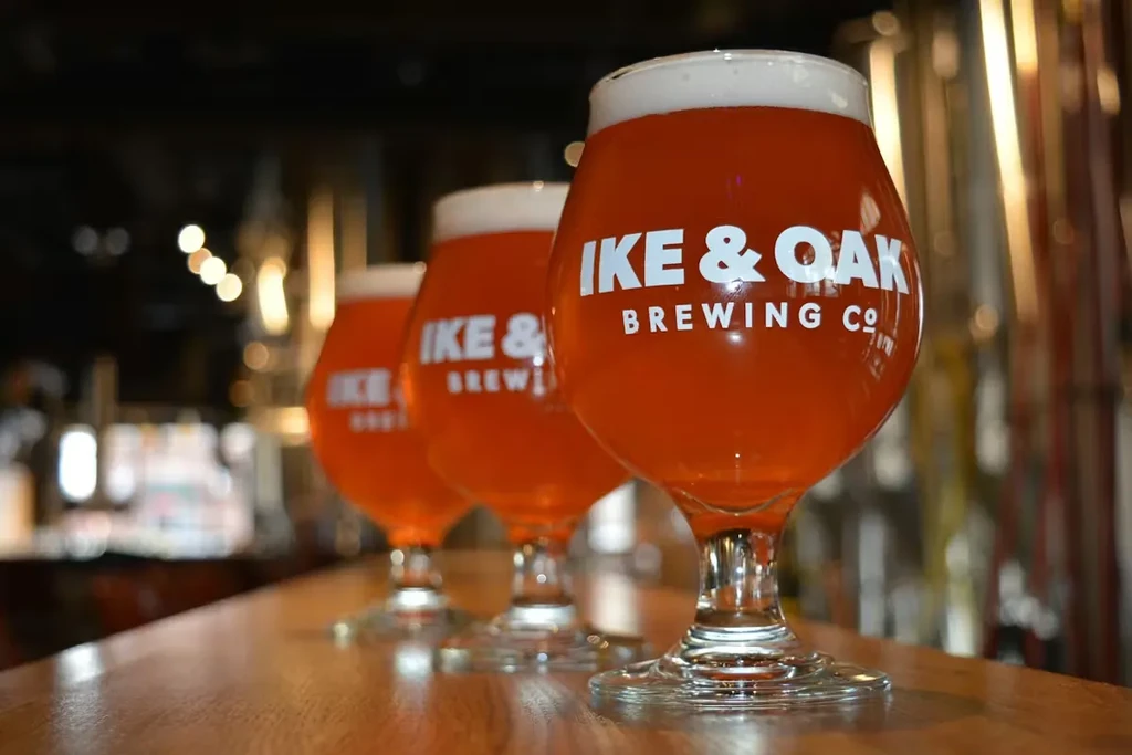 Three stemmed "IKE & OAK BREWING CO" beers on a wooden bar.