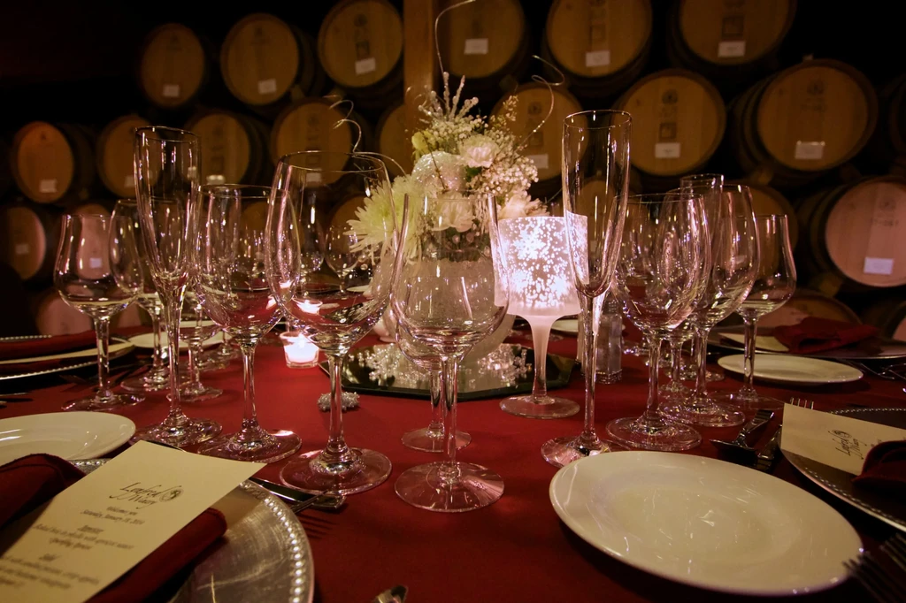 Table set with wine glasses, flowers, candles, red cloth, wine barrels.