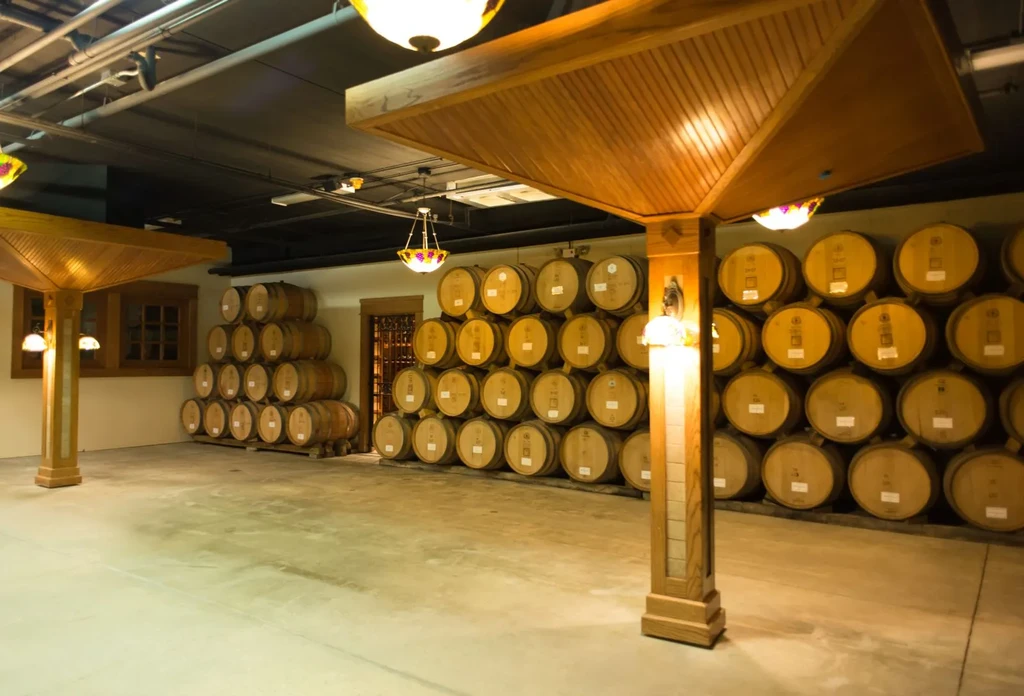 Spacious wine cellar with numerous stacked wooden barrels and ornate lighting.