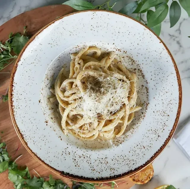 Top-down view: Creamy pasta in white bowl with Parmesan, herbs, lemon.