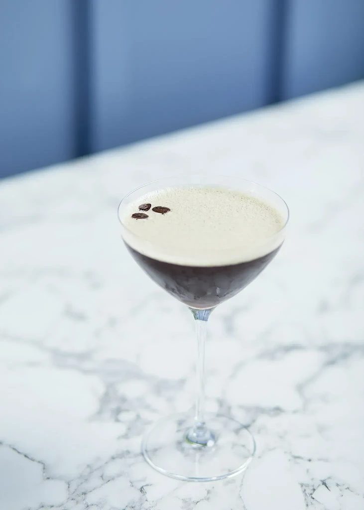 Espresso martini in a martini glass, with foam and coffee beans.