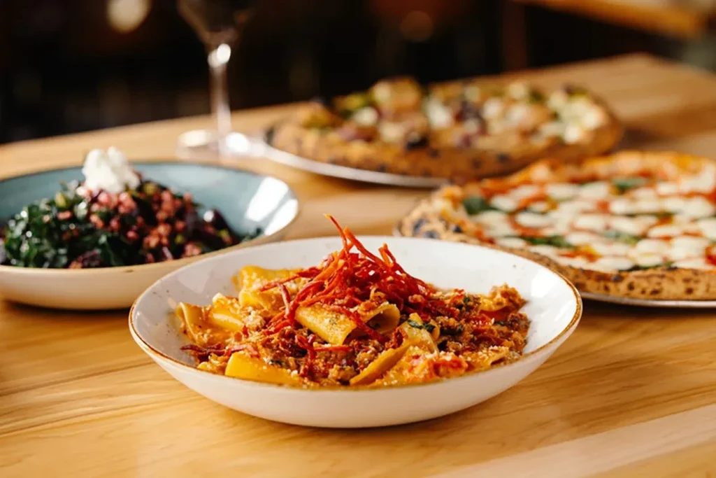 Close-up of pasta, green salad, and pizzas on wooden table.