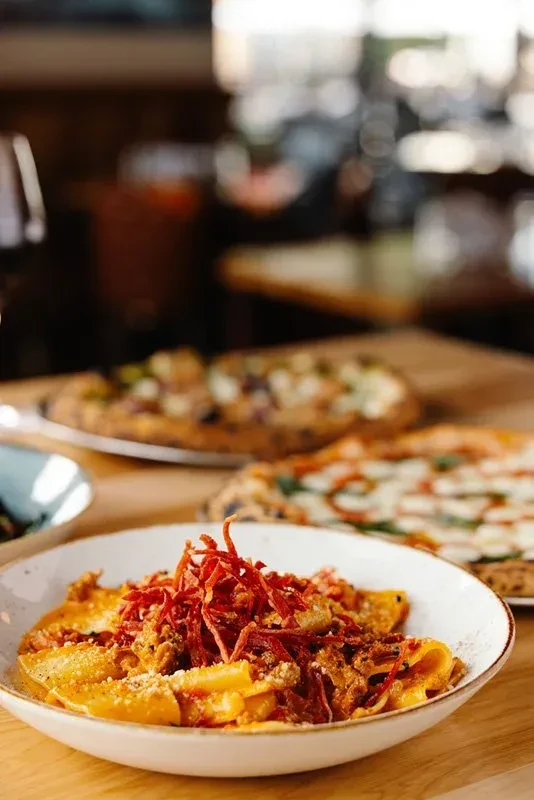 Close-up of pasta with reddish sauce, shredded meat, and grated cheese.