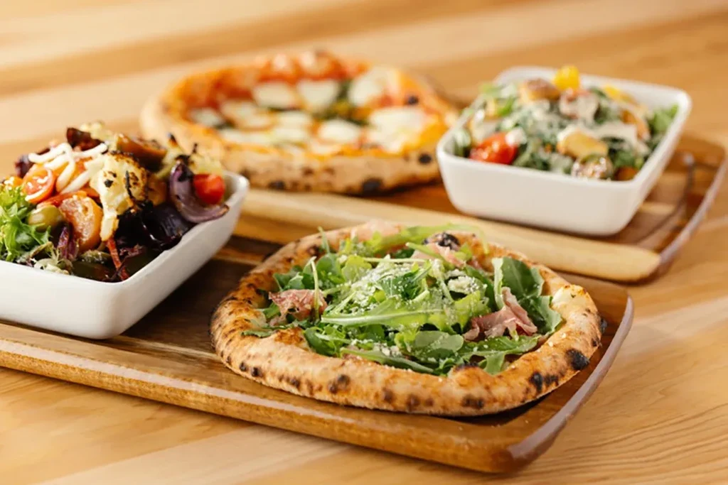 Arugula and margherita pizzas with two salads on a wooden tray.