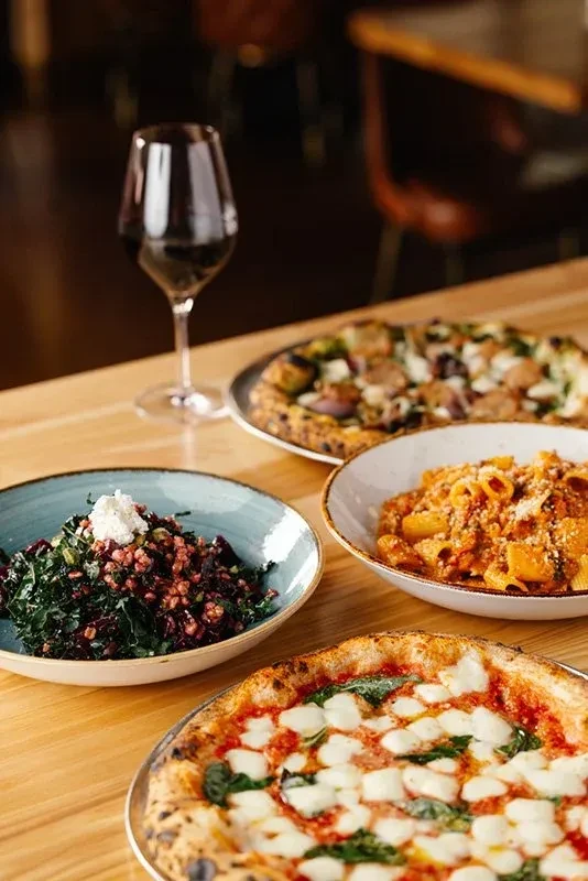 Neapolitan pizza, pasta, salad, and red wine on a restaurant table.