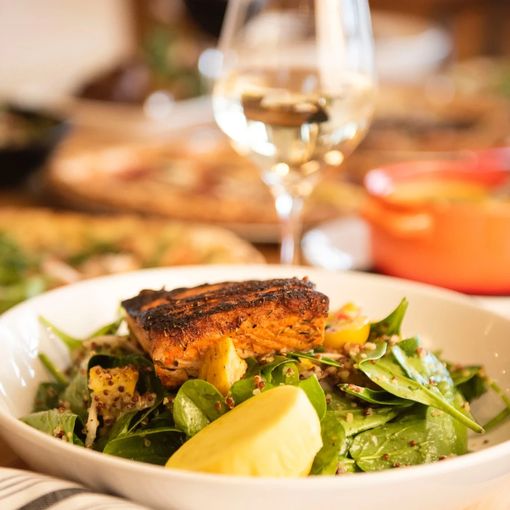 Grilled salmon with spinach, quinoa, mango, and yellow fruit slice.