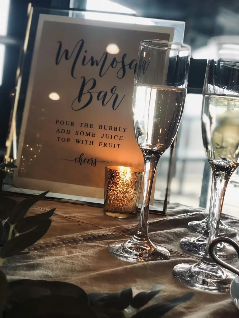 Close-up of Mimosa Bar sign, champagne flutes, and glowing candle.