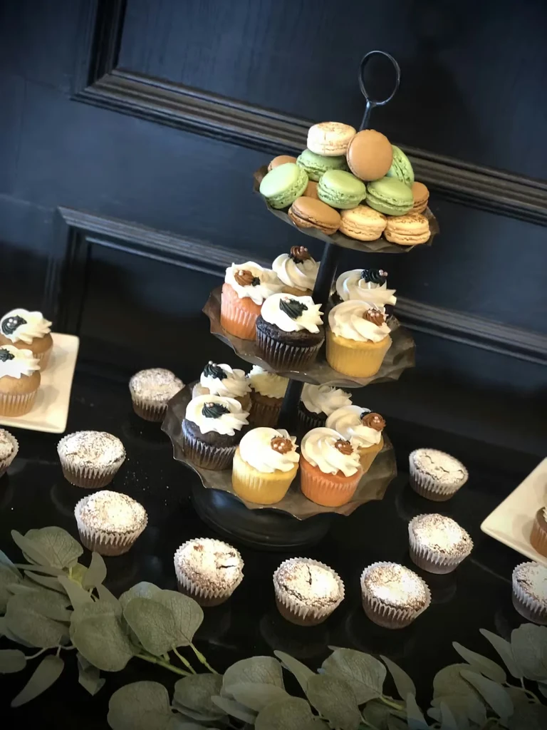 Tiered stand displaying colorful macarons, cupcakes, and powdered mini muffins.
