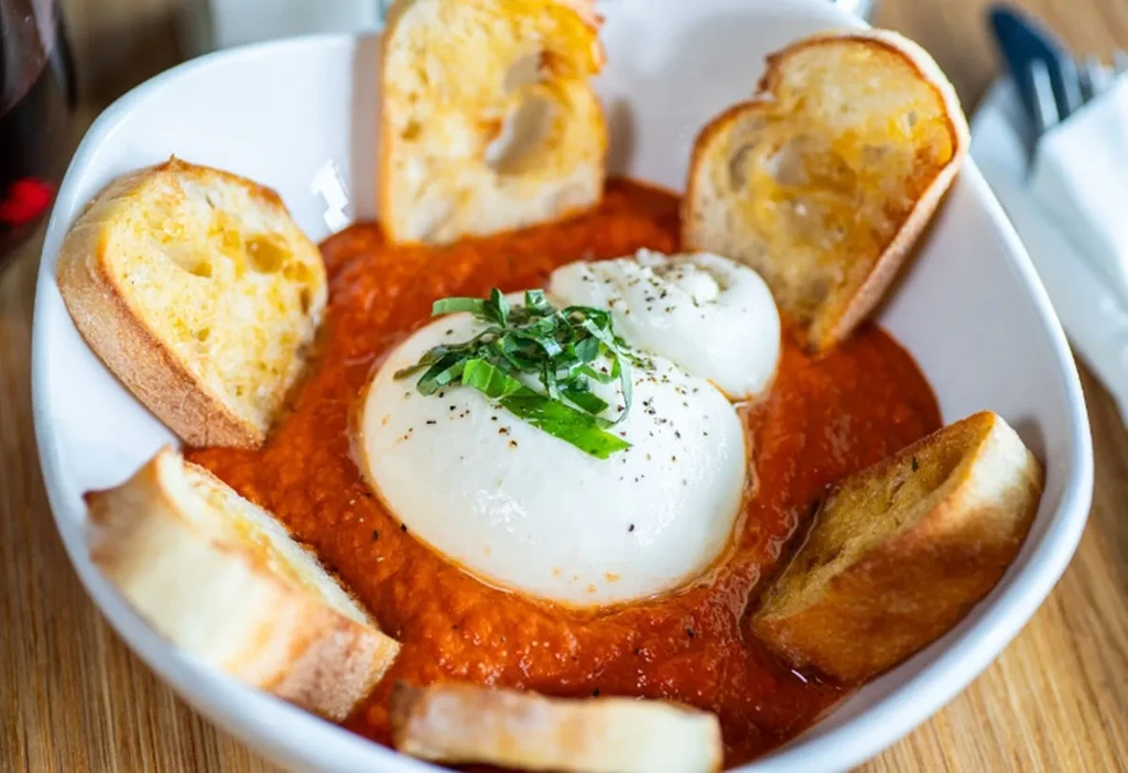 Burrata cheese with basil, pepper, and bread in tomato sauce.