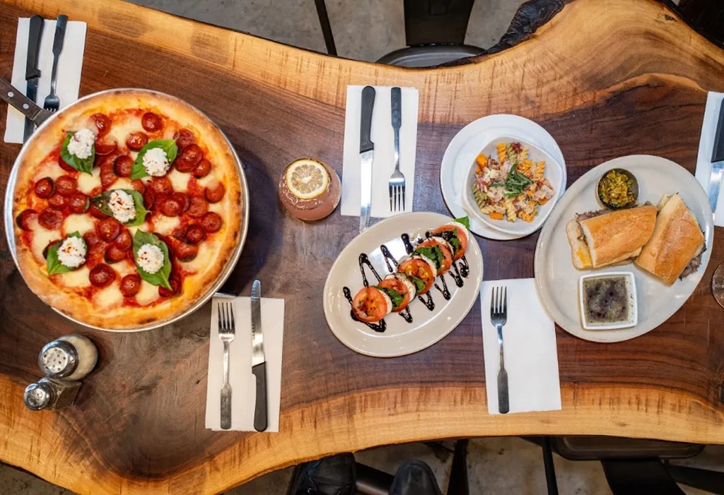 Live-edge wood table laden with pepperoni pizza, salads, and drinks.