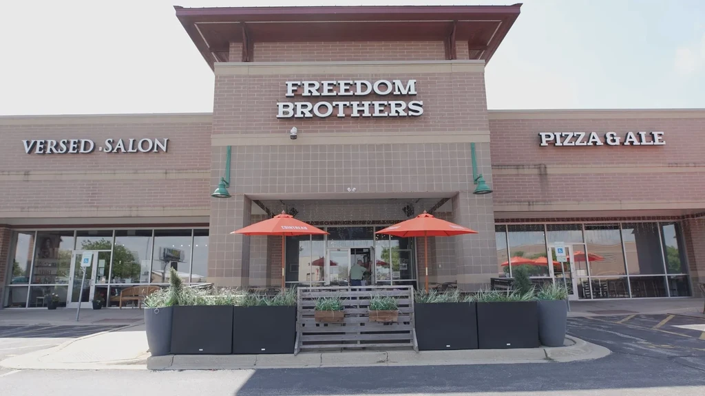 Exterior of Freedom Brothers restaurant with patio, orange umbrellas, and greenery.