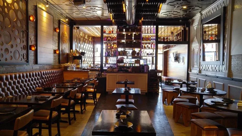 Empty stylish restaurant interior with leather banquette, tables, and lit bar.