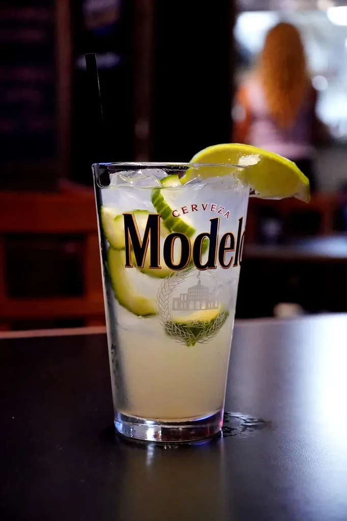 Cold drink with cucumber and lime in a Modelo glass.