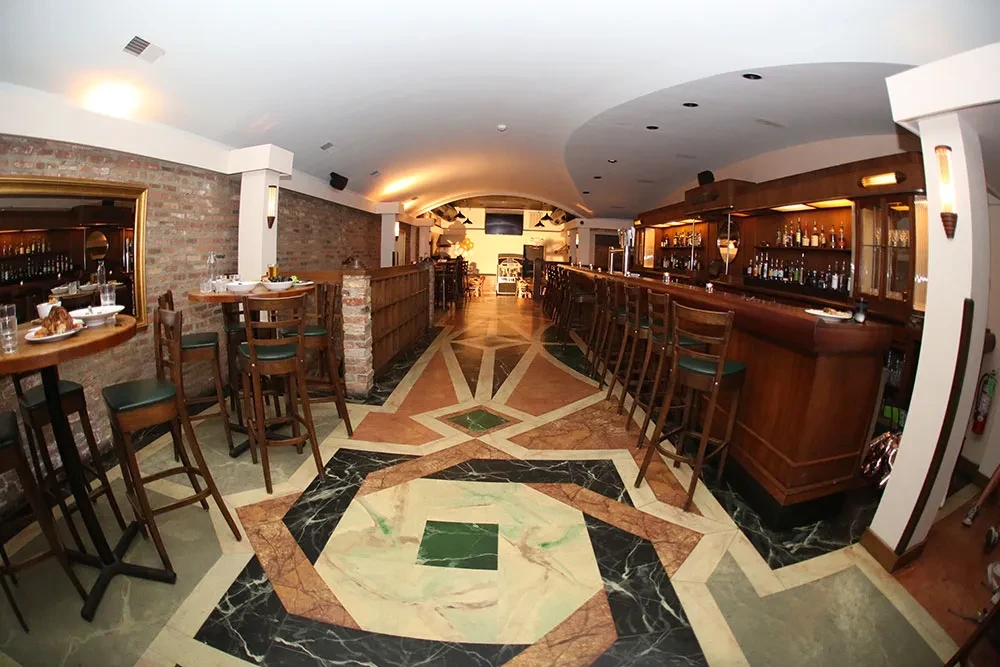 Interior of a restaurant bar with a patterned floor and high-top tables.