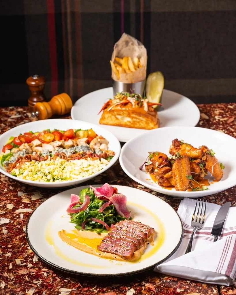 Four plates of tuna, salads, and chicken on a restaurant table.