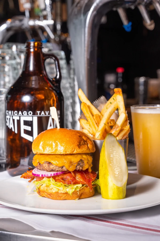 Gourmet burger, fries, pickle, and beer on a white plate.