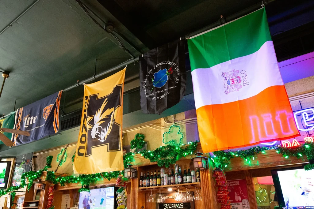Bar interior with multiple flags, festive decor, and bottled beverages.