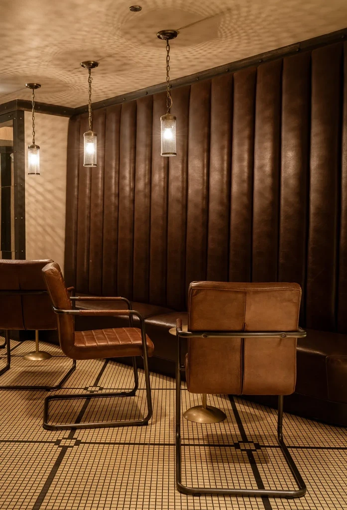 Restaurant interior with brown booths, leather chairs, and pendant lights.