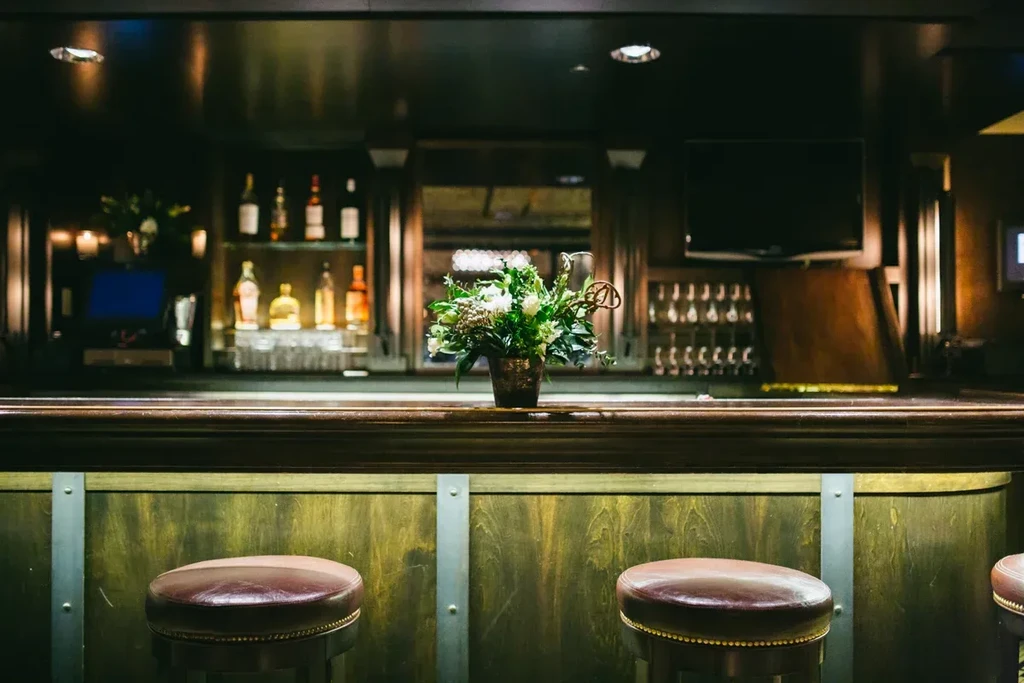 Dimly lit bar interior with a wooden counter and leather stools.