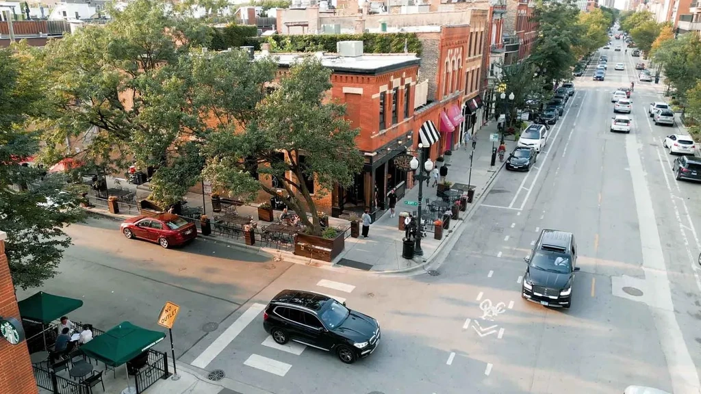 Elevated view of a bustling street with outdoor dining, cars, and pedestrians.