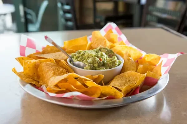 Tortilla chips and guacamole on a metal platter.