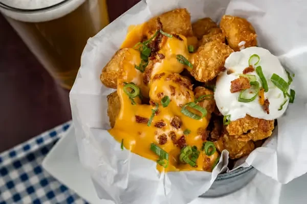 Loaded tater tots in a metal bucket with beer in background.