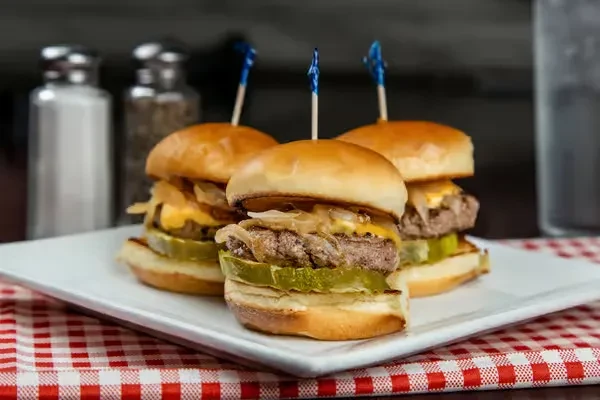 Three mini cheeseburger sliders on a white plate with blue toothpicks.