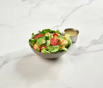 Fresh salad with tomatoes and dressing in a dark grey bowl.