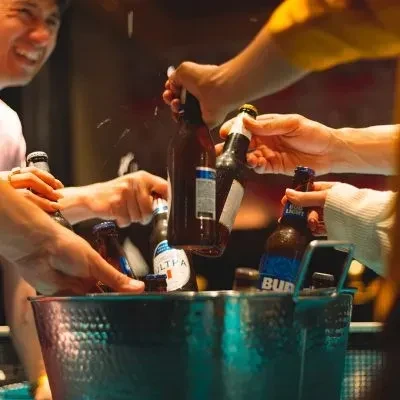 Hands reach for beer bottles in a metallic ice bucket.