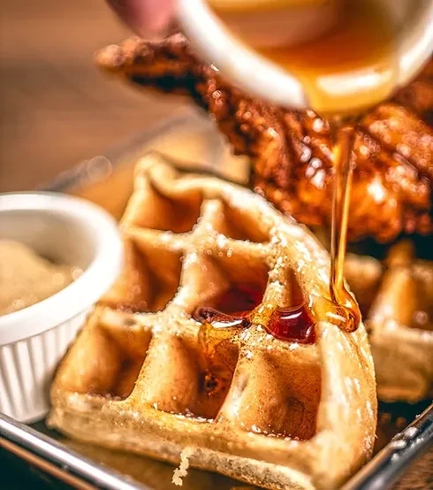 Syrup drizzled over a golden-brown waffle with chicken and dipping sauce.