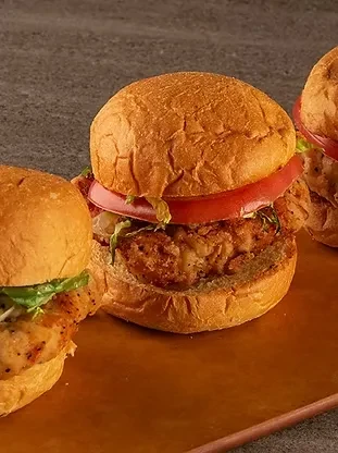 Three burgers, one with fried patty, on a wooden board.