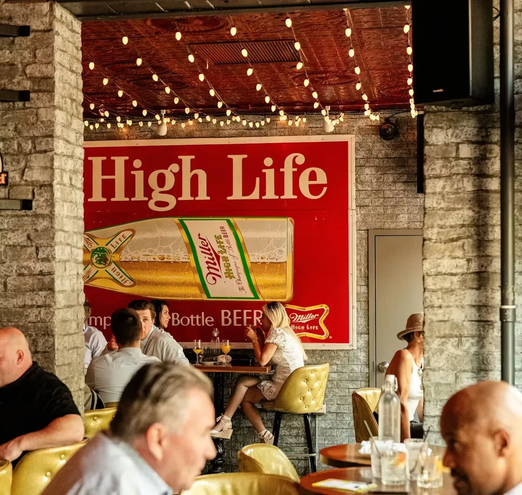 Indoor-outdoor bar scene with patrons and a prominent "High Life" sign.