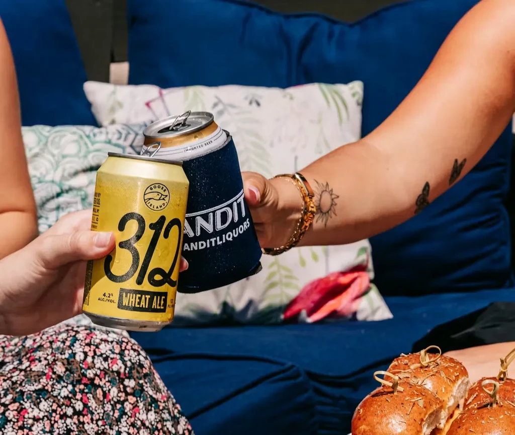 Two people clink beverage cans; one wears a floral dress.