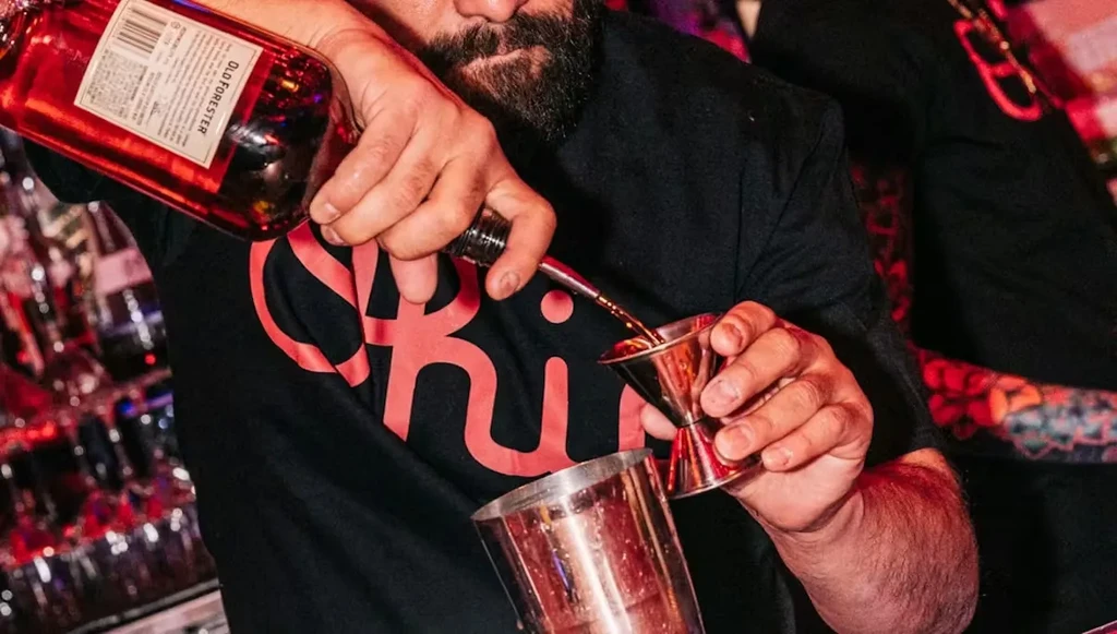 Bartender pours Old Forester whiskey into a jigger.