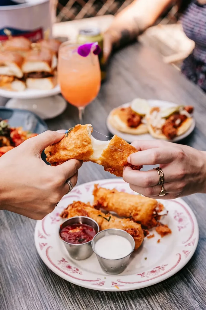 Hands pull apart a deep-fried food item, stretching melted cheese.