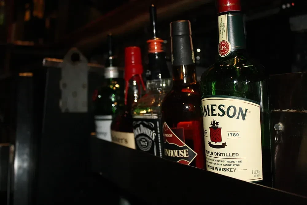 Close-up of Jameson, Jack Daniel's, and other liquor bottles on a dim bar.