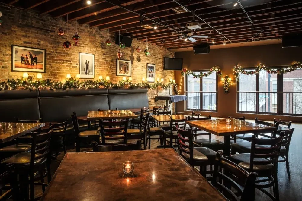 Empty restaurant with reflective tables, dark chairs, and festive decorations.