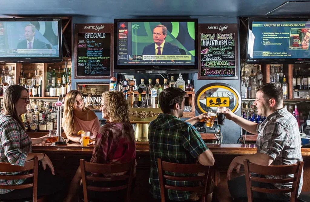 Five people are seated at a wooden bar with many bottles.