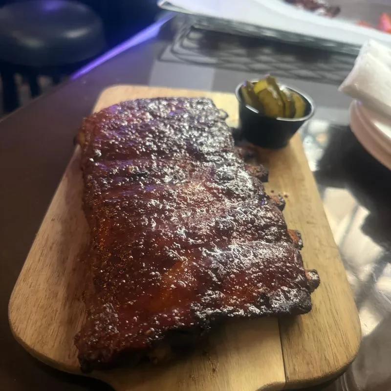Barbecued ribs with sauce and pickles on a wooden cutting board.