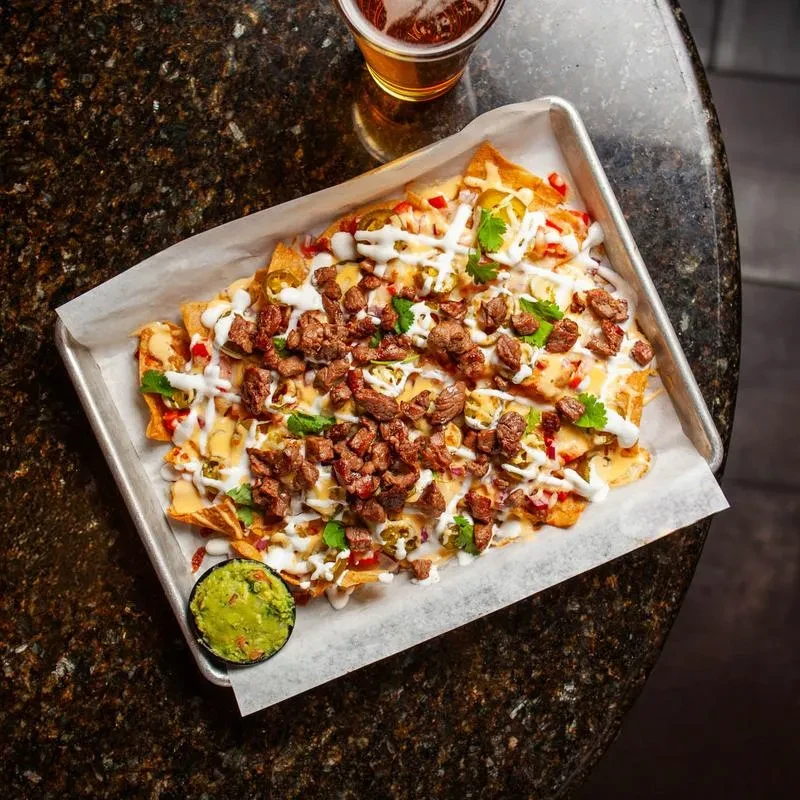 Overhead view of nachos with steak, jalapeños, guacamole, and beer.