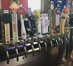 Close-up of numerous beer and cider tap handles at a bar.