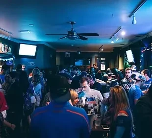 Crowded bar interior with blue and purple lighting.