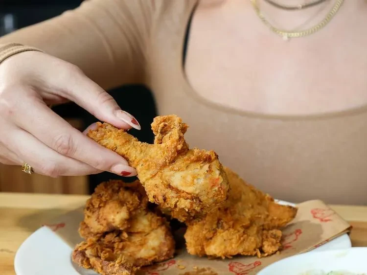 Hand holds crispy fried chicken over a plate of more chicken.