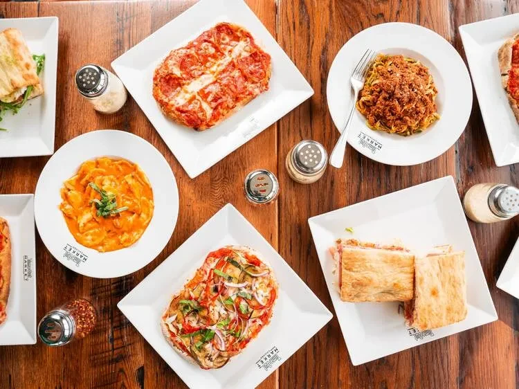 Overhead view of two pizzas, two pastas, and a sandwich on a table.