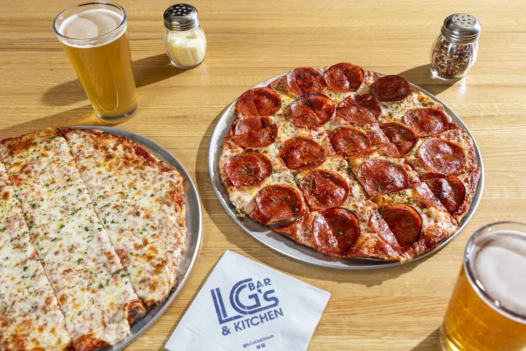 Overhead shot of two square-cut pizzas on a wooden table.