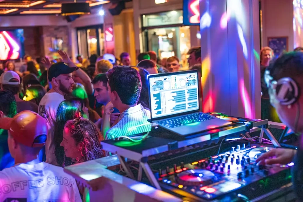 DJ in headphones mixing music for a dense, colorful club crowd.